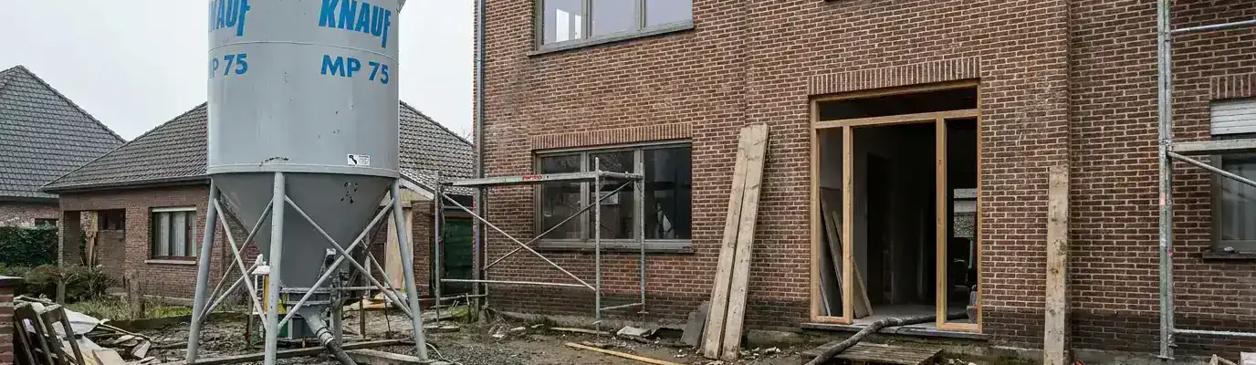 Pleistersilo op de oprit van een nieuwbouwwoning in aanbouw, slang naar de voordeur