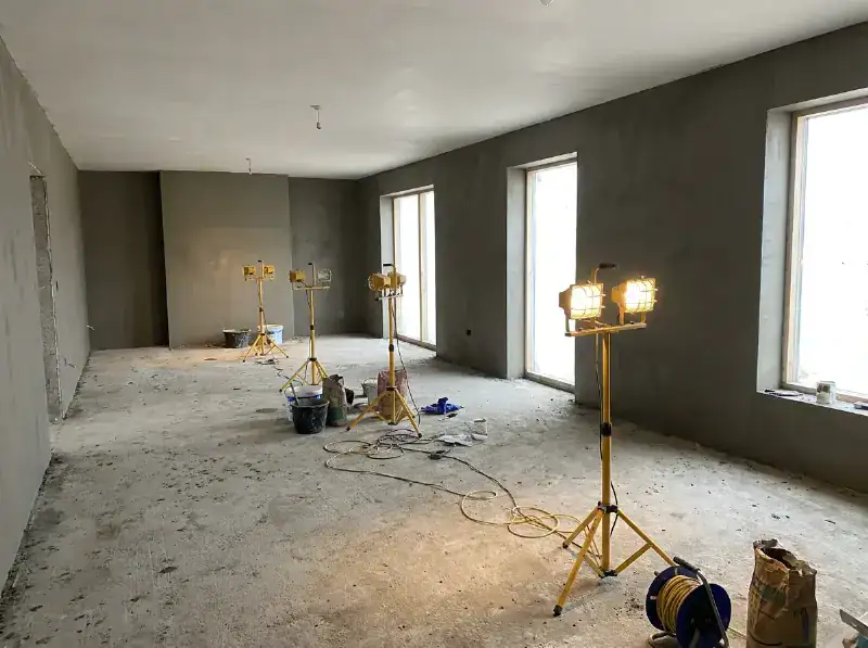 Verdieping van een nieuwbouw in uitvoering, verse raaplaag op alle muren, werflampen aan